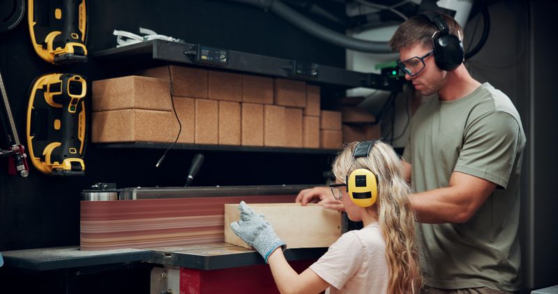 Carpenter, father or kid with woodwork in workshop for carpentry skills, teaching or custom furniture. Manufacturing, dad and girl with wood in garage for learning craft, lumber production or bonding