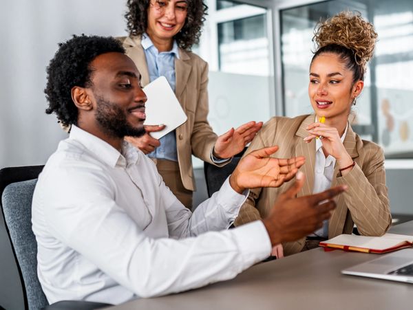 Three professionals engaged in a lively discussion around a table in an office.