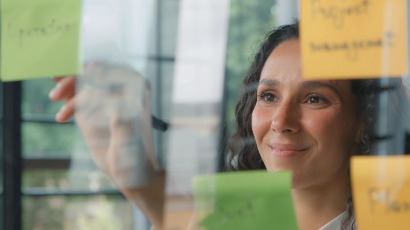 Hispanic woman office business worker write sticky notes writing stickers data information businesswoman female girl creating corporate project tasks working thinking about job plans on glass board. High quality 4k footage
