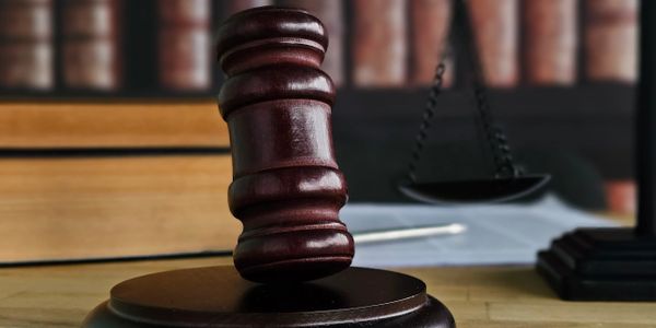 Close-up of a wooden judge's gavel with scales of justice and law books in the background.