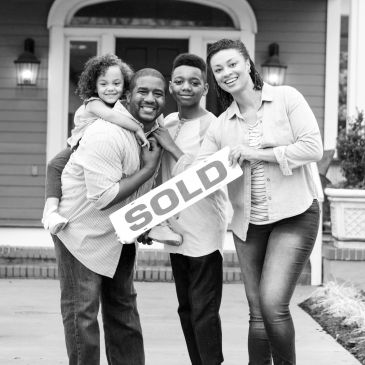 Family celebrating in front of their new home with a sold sign.