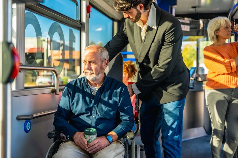 Young man helping a mature man in a wheelchair board a city bus, highlighting accessible public transportation, caring assistance, independence and inclusive urban mobility
