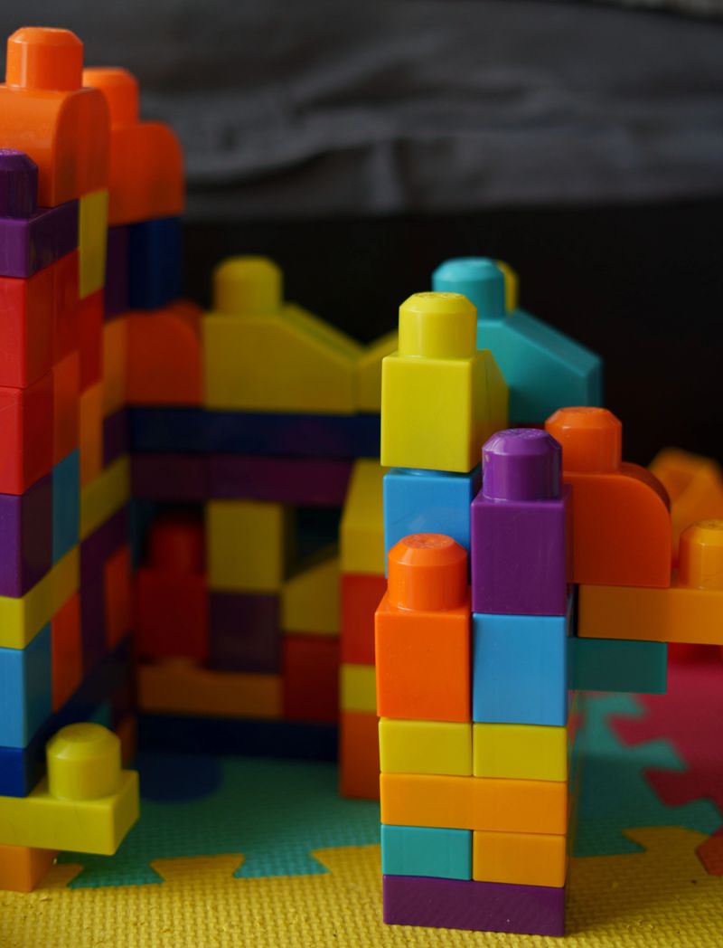 vibrant multicolored building blocks arranged in a playful, intricate structure on a soft foam mat, showcasing creativity and colorfulness in a child's playroom environment, construction