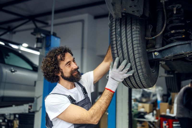 Smiling mechanic working on vehicle, checking and installing a new tire during maintenance in a professional workshop
