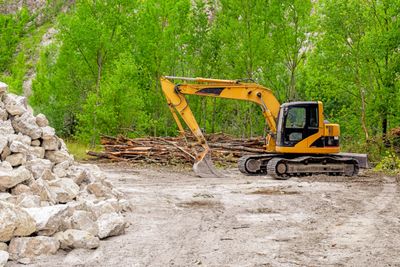 Yellow excavator parked near a pile of rocks in a forest clearing.