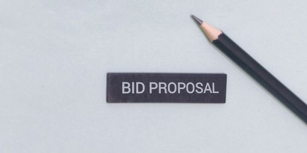A pencil next to a label reading 'BID PROPOSAL' on a white surface.