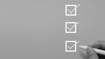 Hand marking checkboxes on a gray surface.