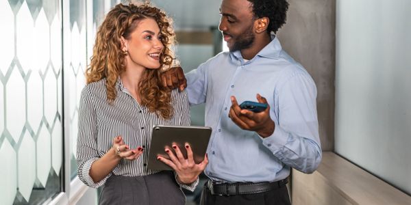 Two coworkers discussing work with a tablet and phone in hand.