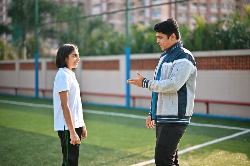 Middle school coach talks with a student on the field, offering support and instructions during physical education class.