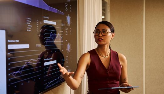 A woman presents data charts on a large screen during a business meeting.
