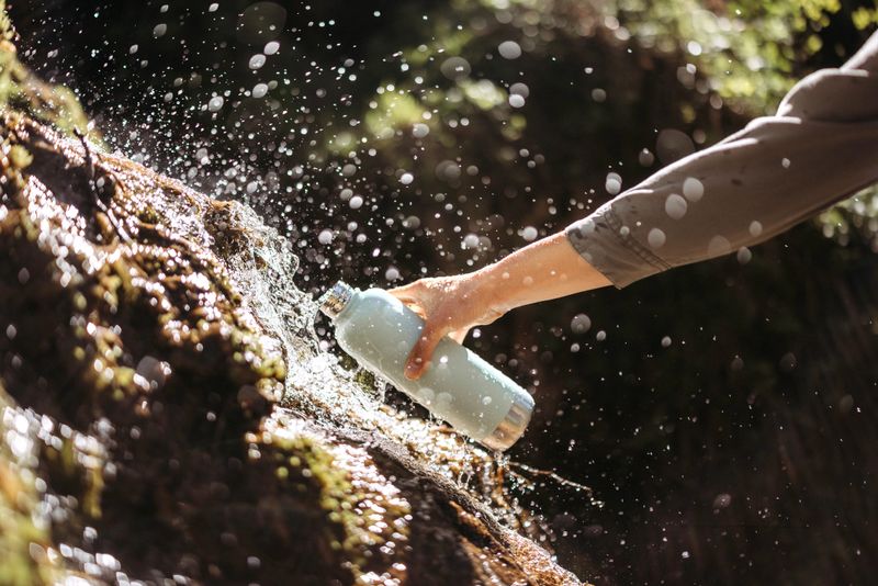 Close up shot of an unrecognisable woman in nature fills up reusable bottle from river waterfall