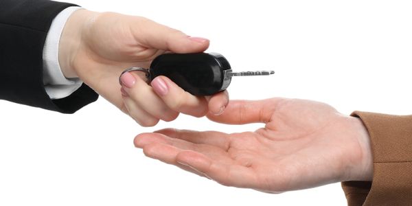 Person handing over a car key to another person.