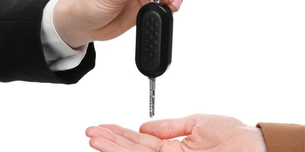Hand passing car key to another hand against white background.
