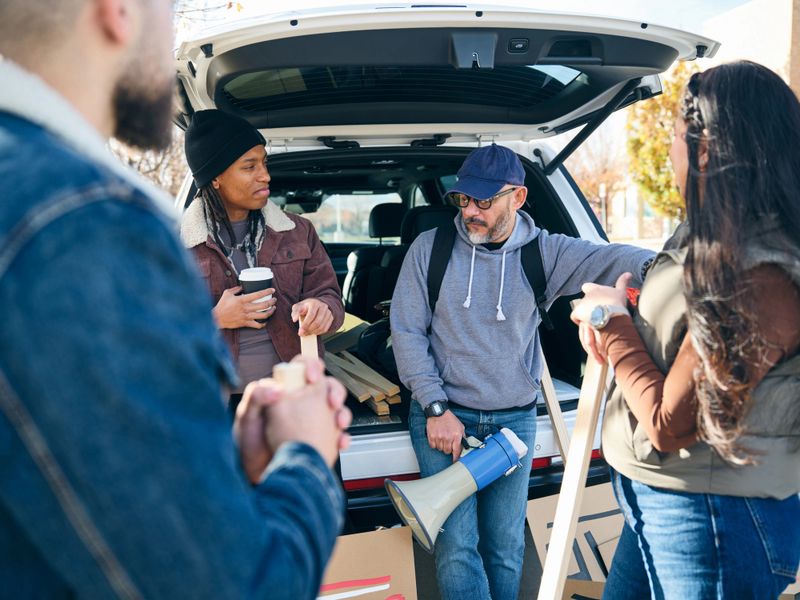 A diverse group of adults gathered outdoors talking and preparing materials for a community project.