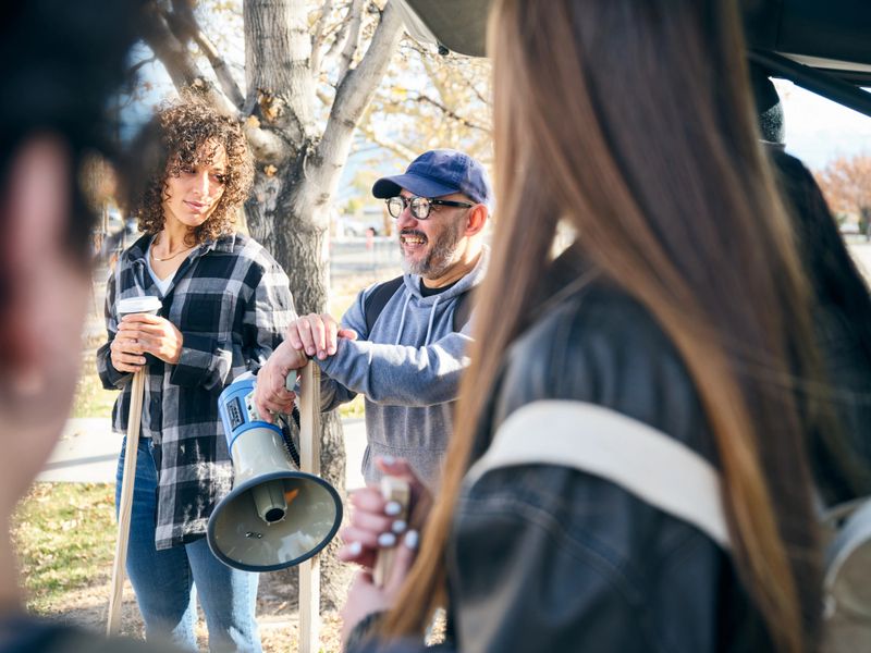 A diverse group of adults gathered outdoors talking and preparing materials for a community project.