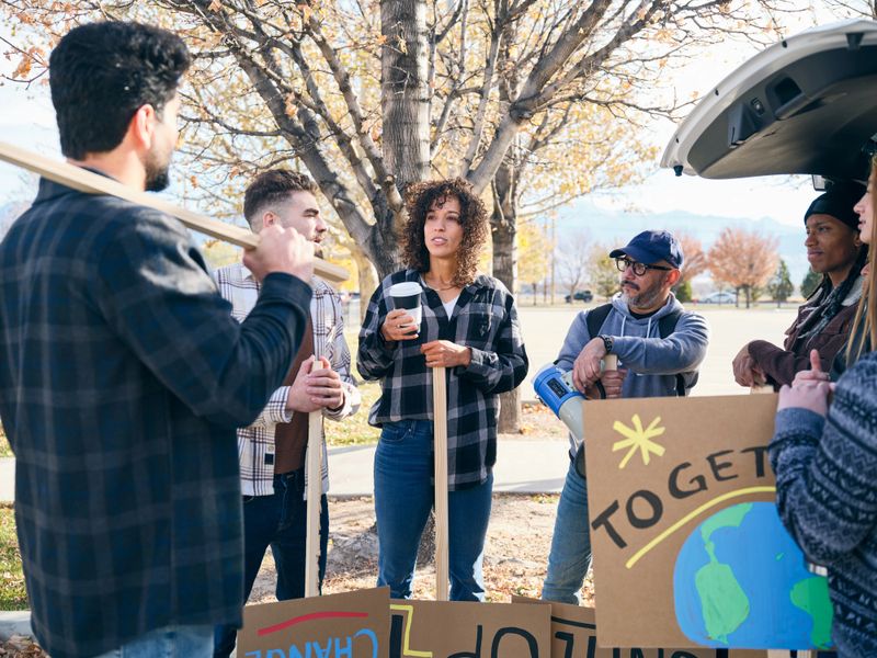 A diverse group of adults gathered outdoors talking and preparing materials for a community project.