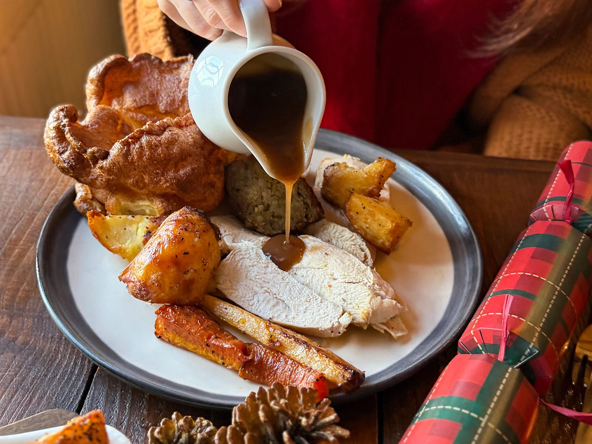 Gravy being poured over sliced turkey and roasted vegetables on a plate.