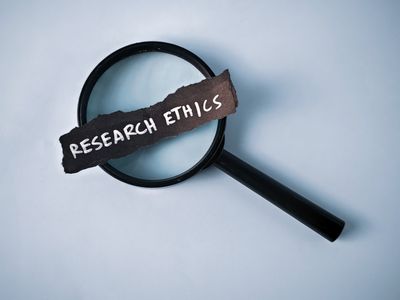 Magnifying glass highlighting the words 'Research Ethics' on torn paper.