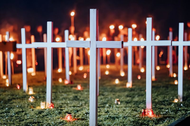 White crosses on grass illuminated by candles and surrounded by people holding torches during a nighttime remembrance ceremony, symbolizing honor and sacrifice
