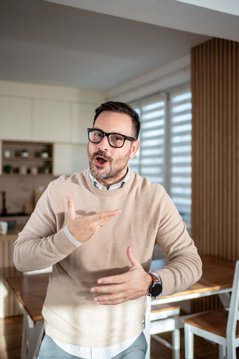 Man with glasses actively explaining and gesturing with his hands, engaging in a lively discussion or presentation while communicating a concept in a casual home environment