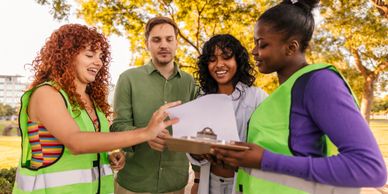 Four volunteers in a park reviewing documents on a clipboard.