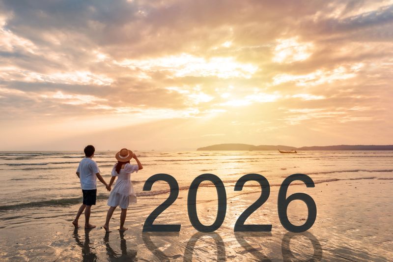 Young woman traveler holding man's hand and looking at beautiful sunset on the tranquil beach celebrating New Year 2024, couple on vacation in summer concept