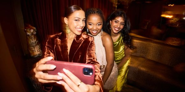 Three women dressed elegantly taking a selfie together at a party.