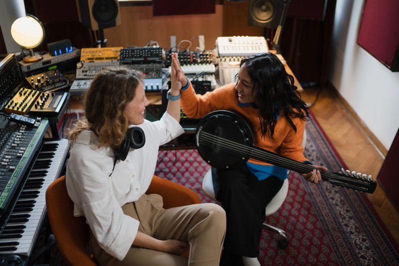 Two women high-fiving while collaborating during a music recording session in a studio