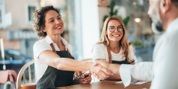 Two women wearing aprons shaking hands with a man across a table.