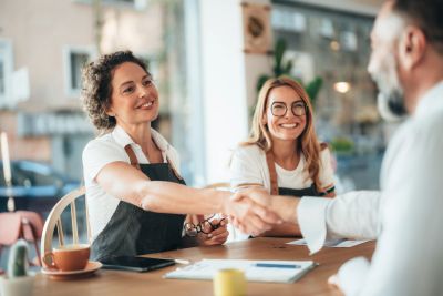 Two women shaking hands with a man in a cafe.