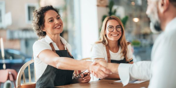 Two women smiling and shaking hands with a man.