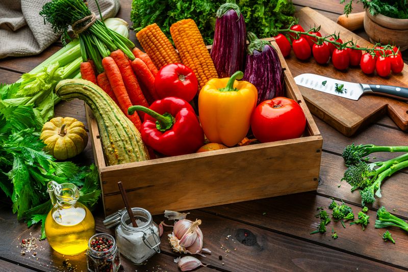 Crate full of fresh organic vegetables on wooden kitchen table. Raw vegetarian ingredients for a healthy diet and wellbeing