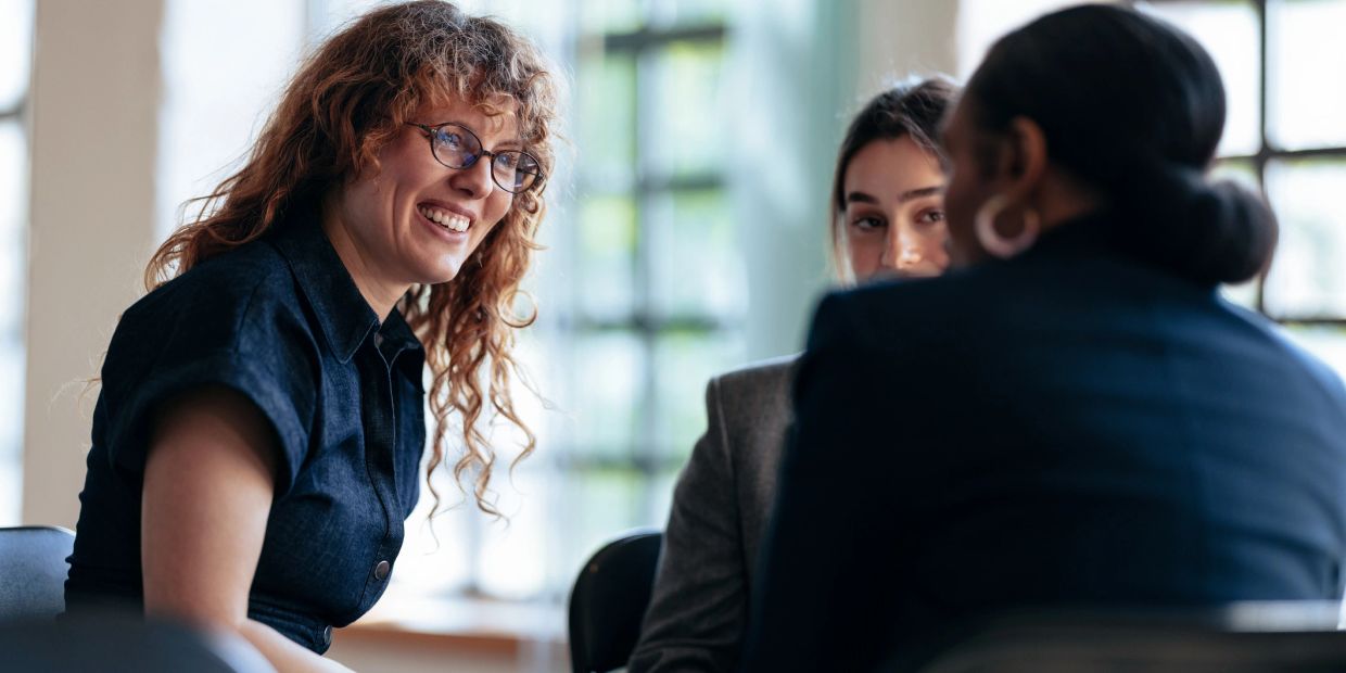 Three women smiling and talking in a bright room.