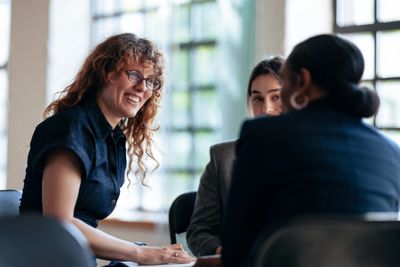 Three colleagues engaged in a cheerful meeting in a bright office.
