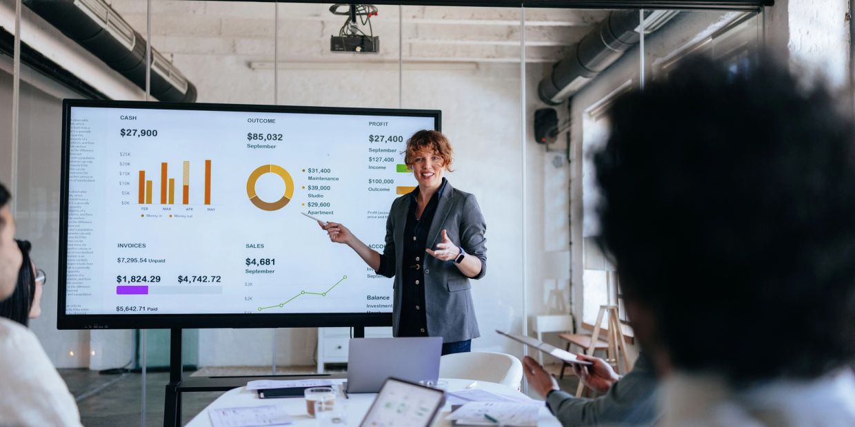 Woman presenting financial data on a large screen in a meeting.