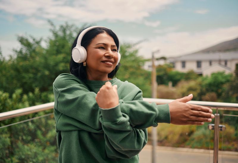 A mature woman stretches her arms and enjoys a refreshing moment of movement and self-care outside.