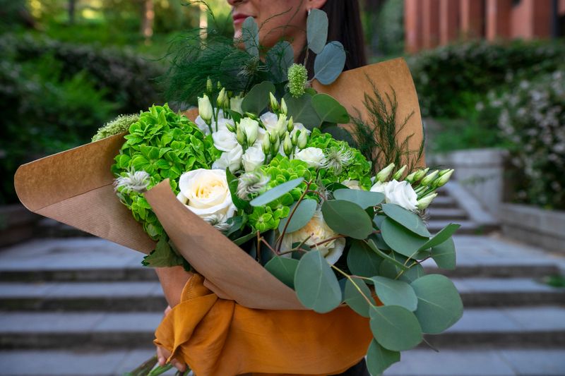 Woman standing outdoors, holding a beautiful fresh bouquet wrapped in kraft paper, delivering flowers for special occasion