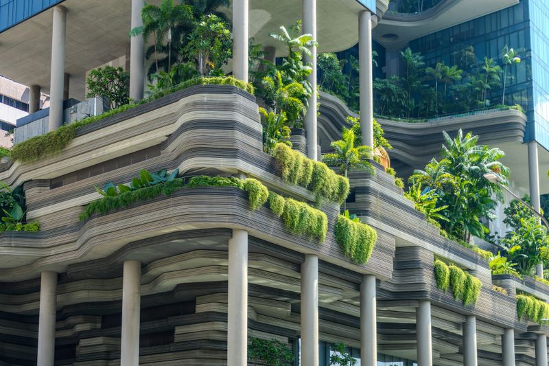 Lush green sky gardens covering the terraced façade of the PARKROYAL on Pickering hotel in Singapore. The building’s distinctive architecture blends modern design with dense tropical vegetation, creating a vertical urban rainforest in the heart of the city. A unique example of sustainable architecture and biophilic design in Southeast Asia