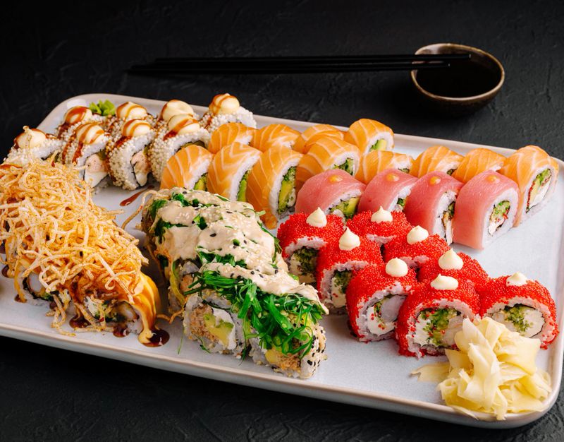A vibrant sushi platter showcases an assortment of sushi rolls, including colorful nigiri, maki, and specialty rolls, adorned with toppings, served on a sleek white plate with soy sauce.