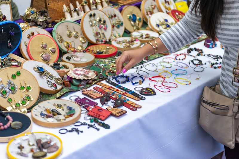 Woman browsing and selecting handmade jewelry from a vendor's display at an outdoor craft fair.