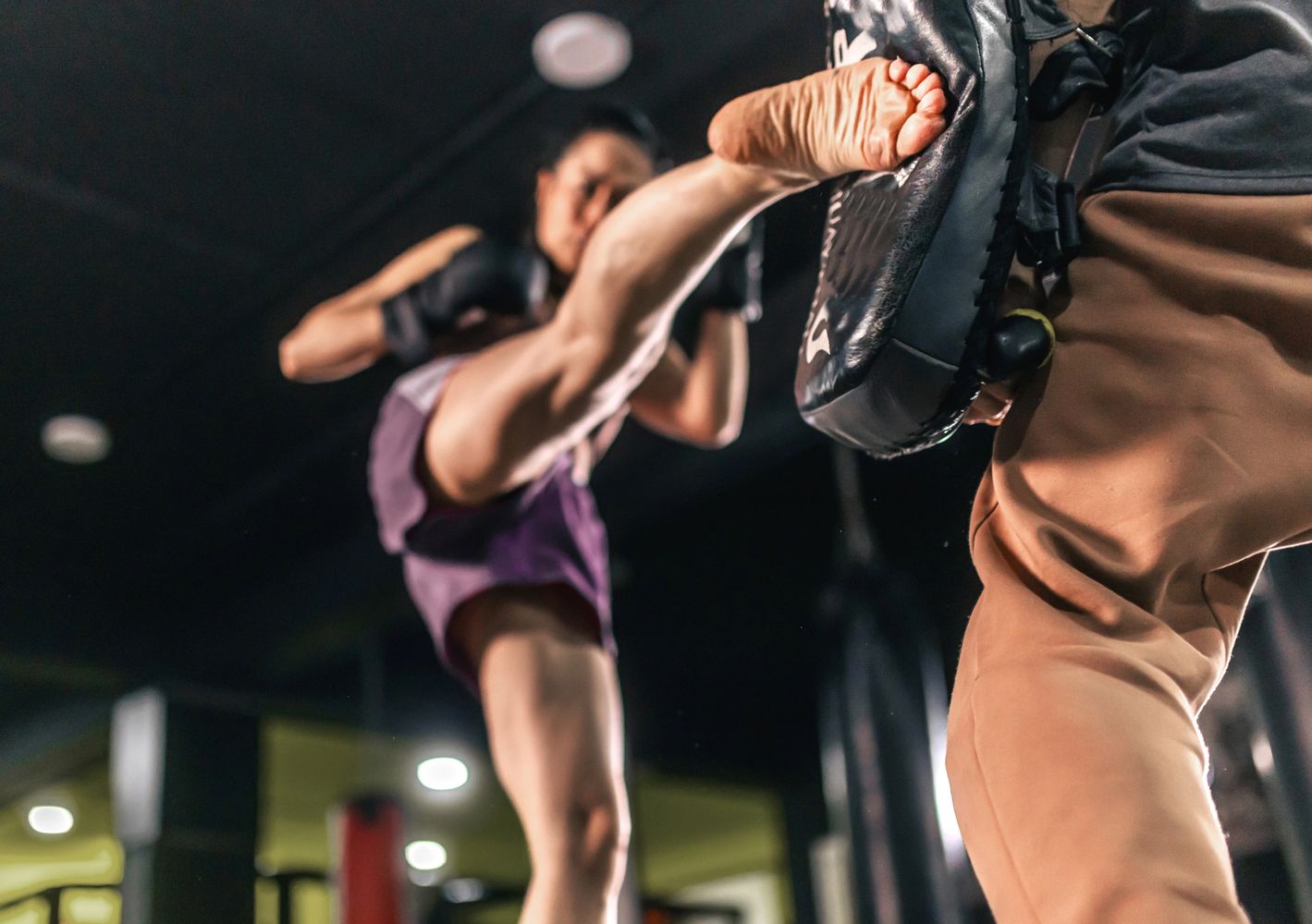 A female martial artist delivering a high kick to a training pad.