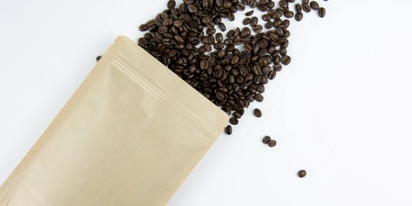 Brown paper bag spilling roasted coffee beans on a white background.