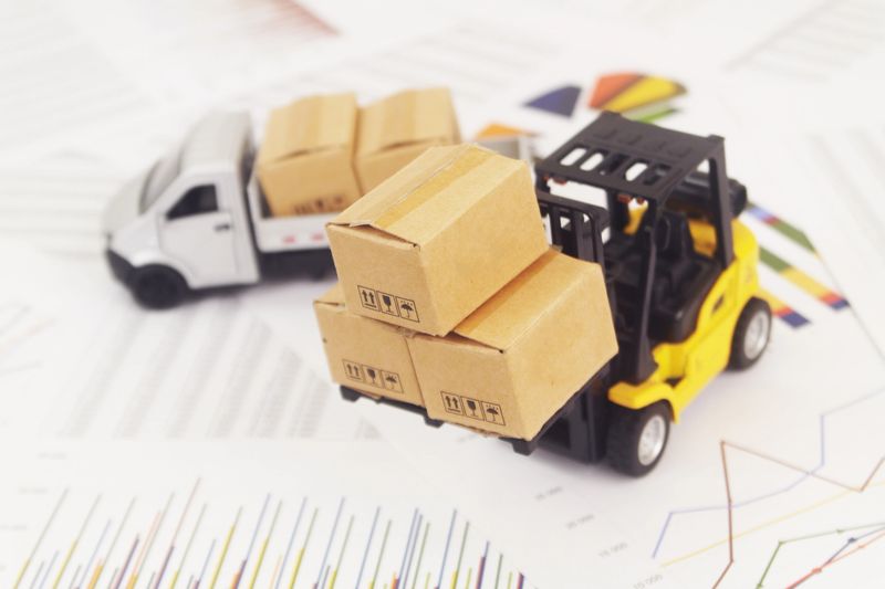 Lorry truck with cardboard boxes and forklift on reports with financial figures. Management of shipping, delivery, cargo, moving and freight transportation concept