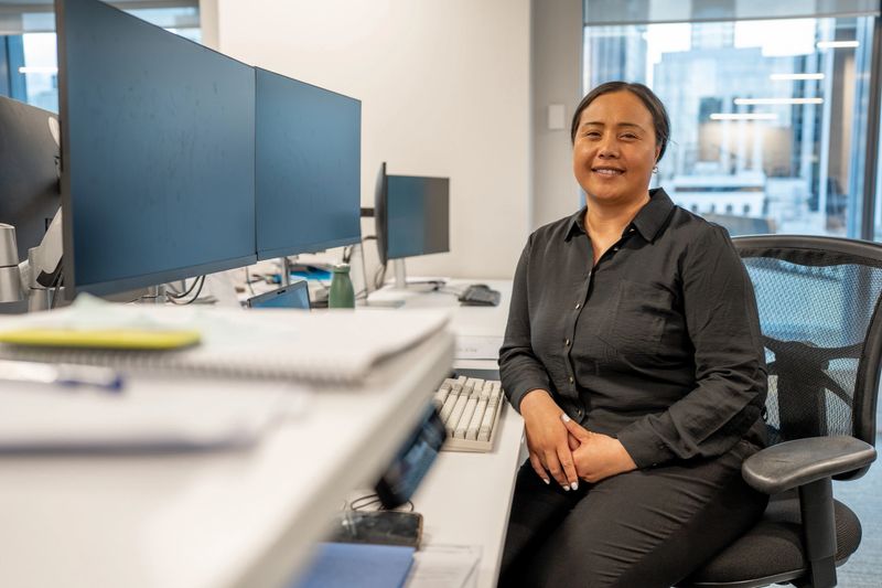 A female professional sitting at an office desk with multiple computer monitors