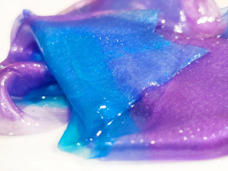 Soft-focus close-up of iridescent purple and blue translucent material, creating abstract flowing shapes with a smooth, shimmering texture.