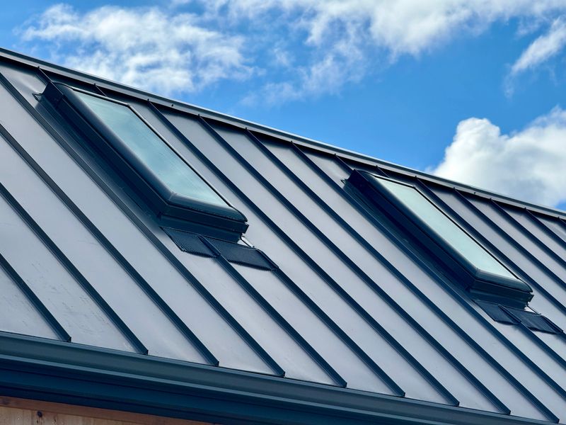 Closeup of attic window on house roof top covered with metal roof.