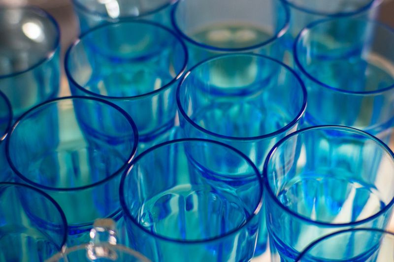 Close-up of empty blue transparent glasses arranged in rows, creating a repetitive geometric pattern with reflections and soft lighting.