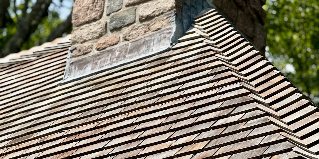 Roof with wooden shingles and a copper cupola under a clear blue sky.