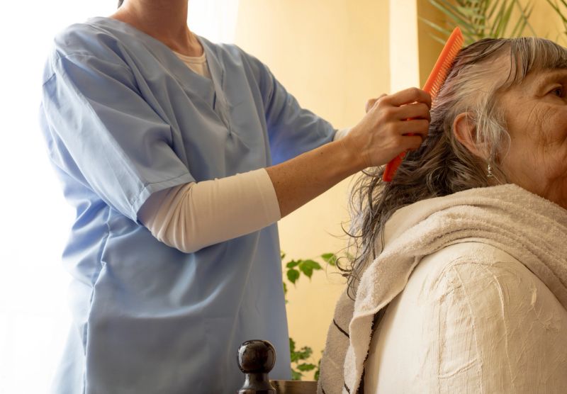 Caregiver is combing a senior woman's wet hair after washing it, providing personal hygiene assistance
