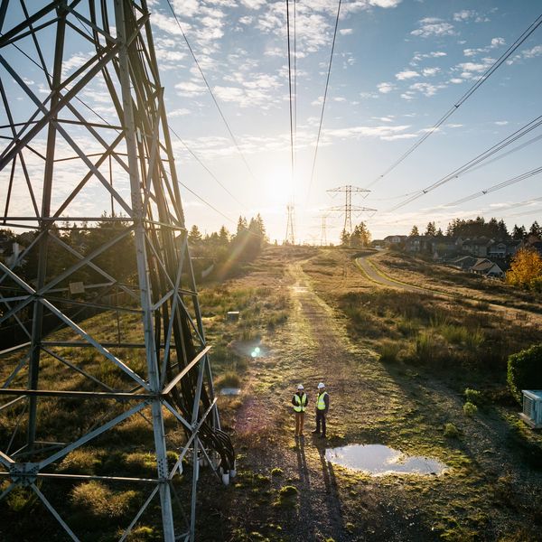 Two workers inspect power lines beneath a sunset-lit sky.